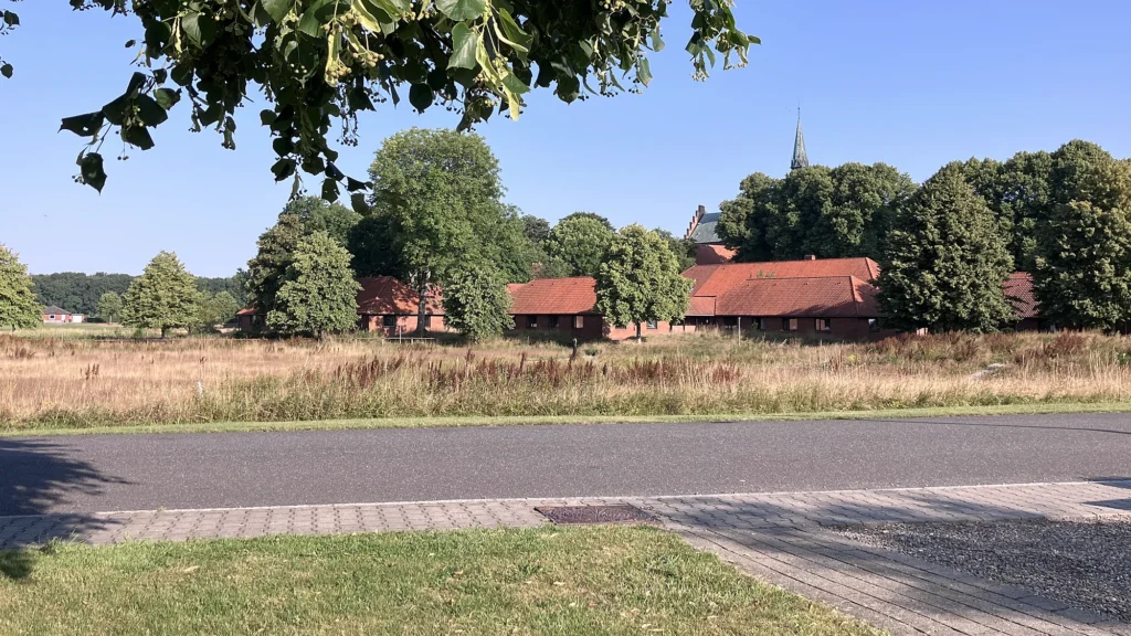 Løgumkloster Refugium med røde tegltage og kirkens spir set over marken fra Sølstedgårdvej, med vejen i forgrunden