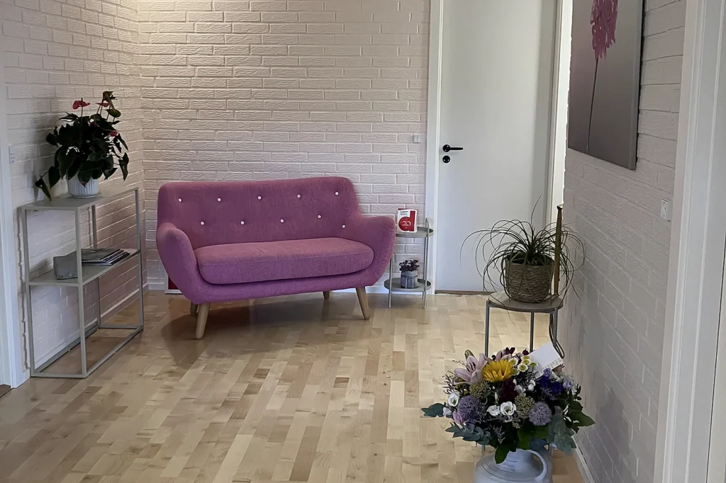 Ventehjørne i klinikken i Løgumkloster med lyserød sofa, plante og en buket blomster