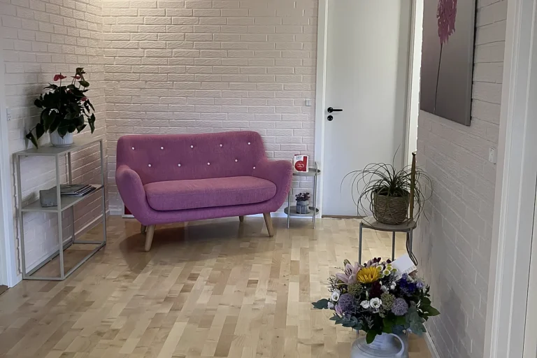 Ventehjørne i klinikken i Løgumkloster med lyserød sofa, plante og en buket blomster